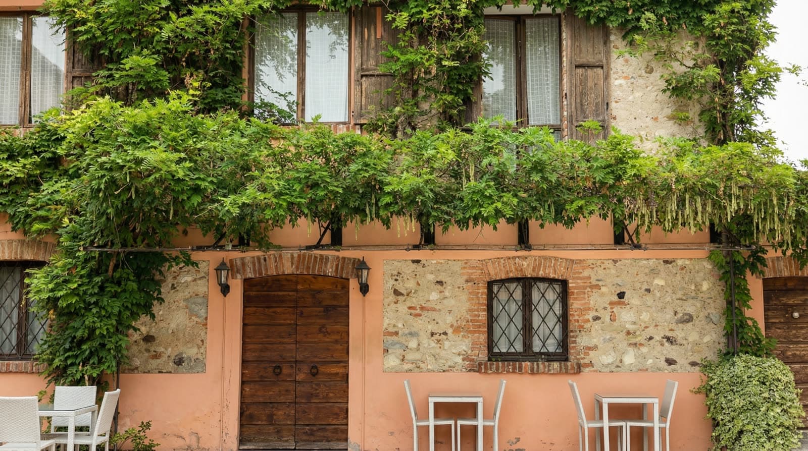 Facciata in pietra di Cascina Feliciana coperta di vite, con tavolini all'aperto